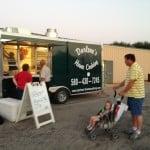 A food trailer is being visited by customers in a parking lot