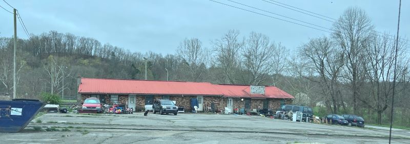 A house that is long and narrow with a metal roof. Piles of trash are stacked in front. 