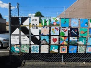 Art squares hanging on the chain link fence in neat rows. 