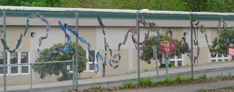 Painted fish shapes hang from a chain link fence