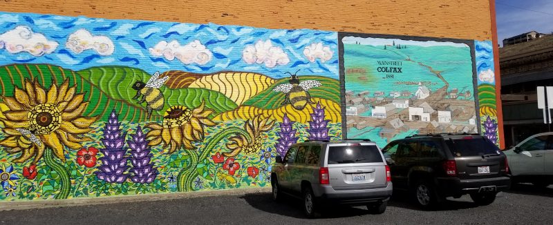 Bright colorful mural showing the landscape around Colfax, Washington, framing a smaller mural of historic Colfax.