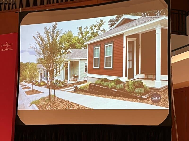 Photo of a row of small houses on a sloping lot. They have tiny yards with cute flower beds and are painted in attractive colors. 