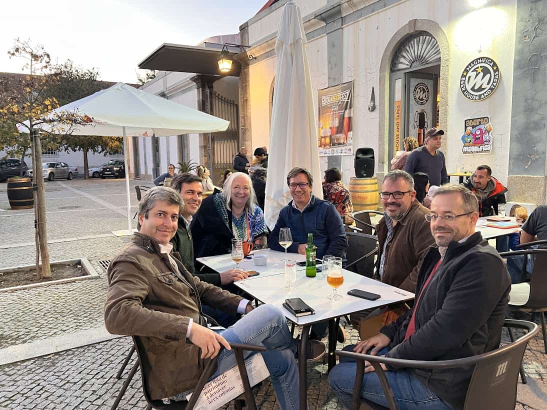A group of people seated at outdoor tables in front of a tapas restaurant in Portugal. They turn and smile for the camera.