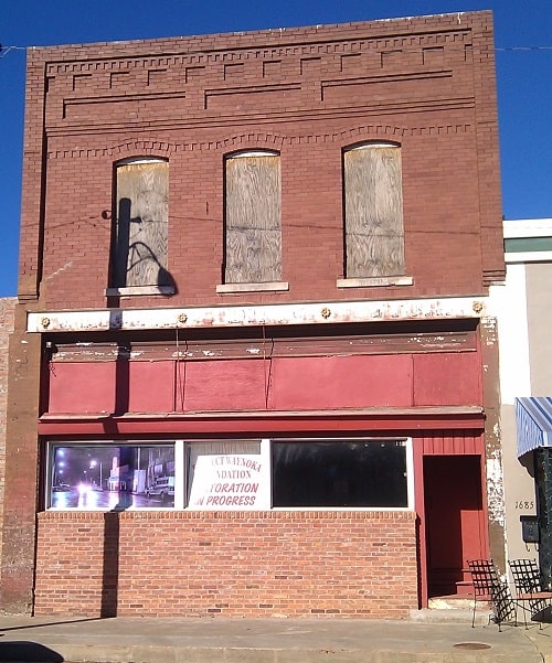 A downtown brick building with boarded up windows. 