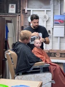 Barbership in Gowrie Iowa young man getting a hair cut while sitting on dads lap