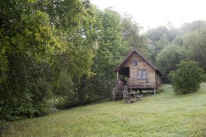 A rustic wooden cabin on a platform stands on a gentle hillside surrounded by green trees. Photo CC by Myles Tan