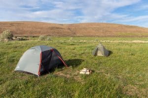 Tents set up in an open green field with mountain foothills at the horizon. Photo CC by Matt Zimmerman