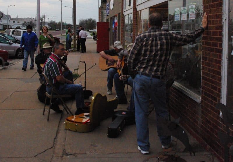 Musicians play on the sidewalk in front of a small retail store. 
