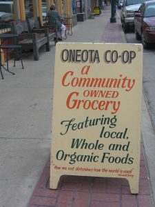 Signboard on a sidewalk says, "Oneota Co-op, a community owned grocery featuring local, whole and organic foods