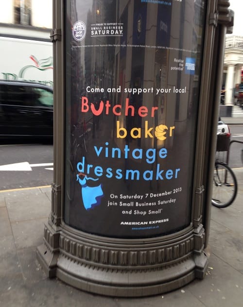 Outdoor advertising banner says, "Come and support your local butcher, baker and vintage dressmaker." 