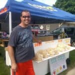 A booth displaying kettle corn in a front yard. The owner is smiling in the foreground