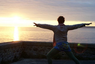 Woman doing yoga at sunrise near the ocean.